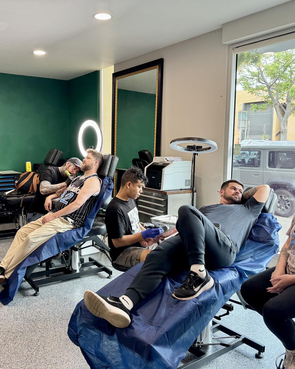 Three artists tattooing clients on the studio floor at Mother Goose Tattoo, Kensington
