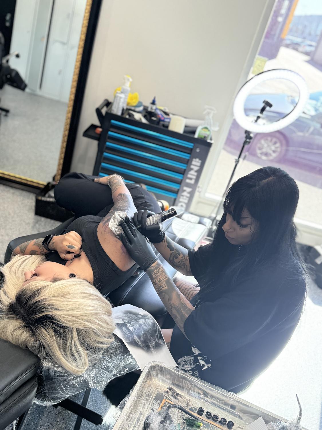An artist tattooing a client's arm at Mother Goose Tattoo, Kensington